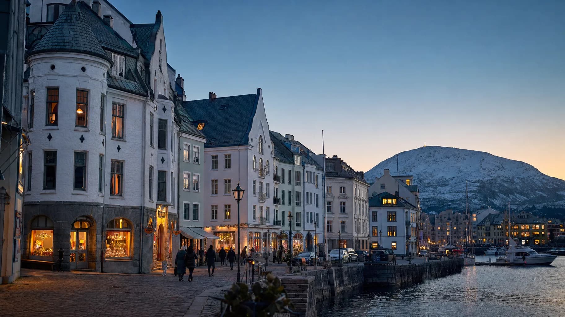 Brosundet i Ålesund i skumringen, med jugendbygninger og snødekte fjell i bakgrunnen